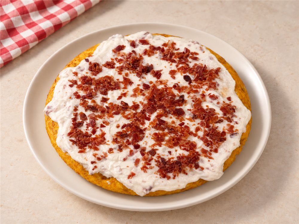 Tortilla cubierta con una capa de alioli y jamón crujiente troceado por encima