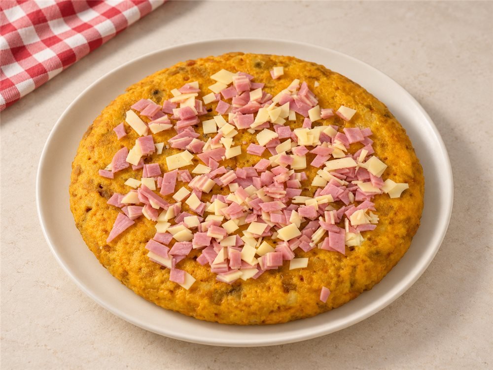 Tortilla abierta con jamón y queso troceados repartidos por encima, lista para rellenar